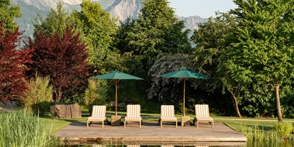 Wellnessurlaub - Biosauna - Isny im Allgäu - Blick auf die Berge und im Vordergrund Liegestühle am Bergsee. - Sonnenalp Resort
