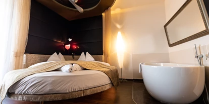 Wellnessurlaub - Restaurant - Stegersbach - Kuschelige Stunden erwarten Sie in unserem Fantasy Room mit 25m². Die Zimmer sind in modernem, italienischen Stil eingerichtet. Highlights des Fantasy Rooms sind mit Sicherheit das große runde Deluxe-Kuschelbett (235cm) mit exklusiver „Seally“ Luxusmatratze und die freistehende Design-Badewanne im Zimmer. Geboten wird ein modernes, italienisches Badezimmer mit „Rainshower-Dusche“ und einem separatem WC. Ein Balkon mit Kuschelbankerl sorgt für romantische Stunden zu zweit. Sollte es heiß hergehen, sorgt eine Klimaanlage für die nötige Abkühlung. Eine Minibar, ein elektronischer Safe und ein LED TV mit Blu-Ray Player runden das Angebot ab. - Maiers Kuschelhotel Loipersdorf Deluxe