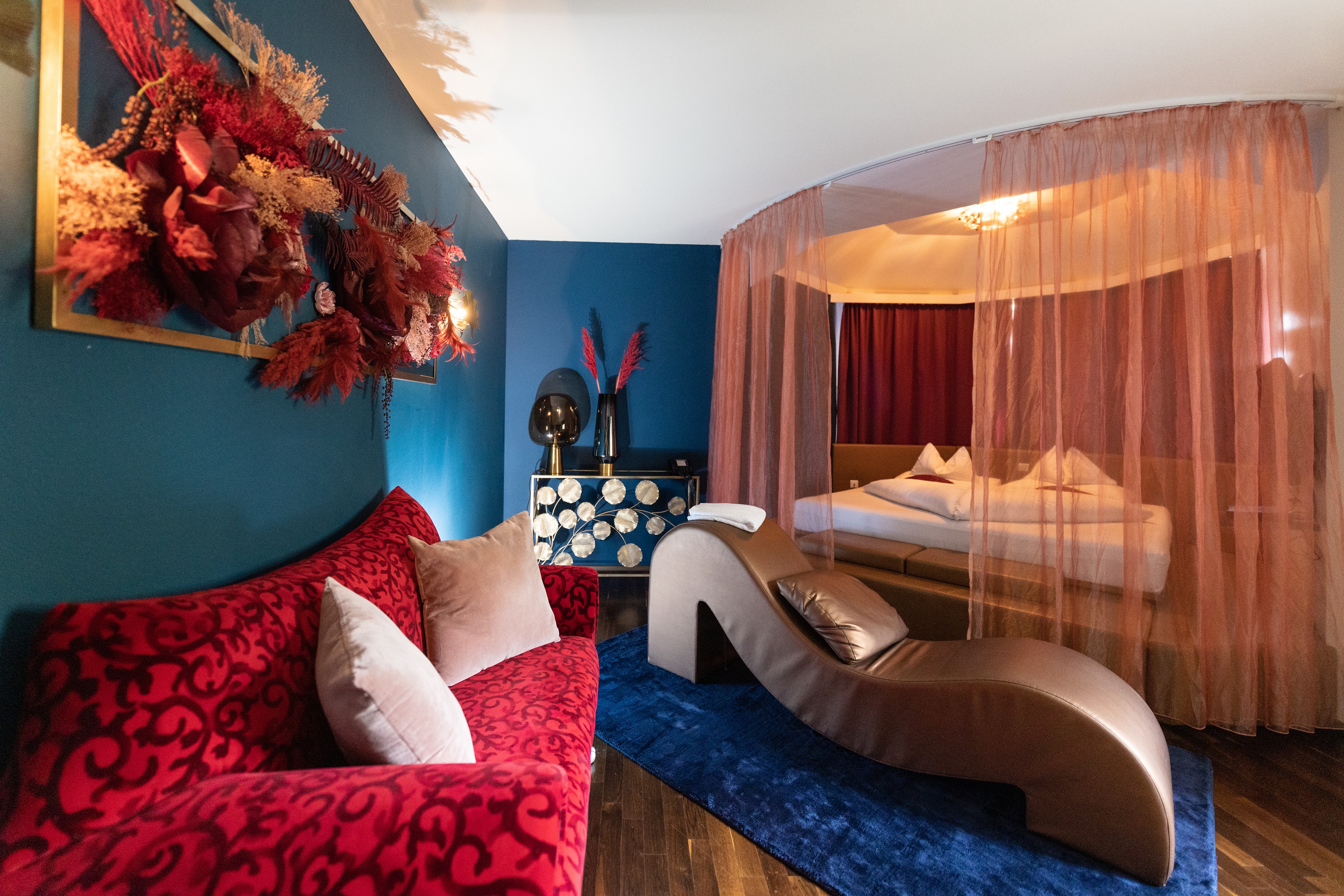 Wellnesshotel: Grand Penthouse Paradise Suite 
Das ultimative Luxuserlebnis erstreckt sich über 90 m², auf zwei Etagen, verbunden mit einer Marmor-Wendeltreppe. Modernes, italienisches Design und das Ambiente sorgen für romantische Momente. Im Obergeschoß sorgt ein großes Kuschelbett für prickelnde Stunden zu zweit. Das „Open-Space“ Badezimmer bietet einen Air-Pool, eine große Dusche, einen Fön und ein separates WC. Die zweistöckige Suite bietet eine finnische Sauna von „Klafs“ mit Blick in den Wohnbereich. Mehrere LED TVs mit Blu-Ray Player sorgen zusätzlich für Unterhaltung. Vom großen Balkon der Suite haben Sie perfekten Blick auf den Liebesgarten, sowie auf die Therme Loipersdorf. Für zusätzliche Romantik sorgen ein elektrischer Zimmerkamin, sowie ein „Bretz“ Kuschelsofa. Die Klimaanlage sorgt für die nötige Abkühlung nach heißen Stunden. Weiters bietet die Suite eine Zimmerbar mit Kaffeemaschine und einen Zimmersaf - Maiers Kuschelhotel Loipersdorf Deluxe  - Zimmer | Suiten