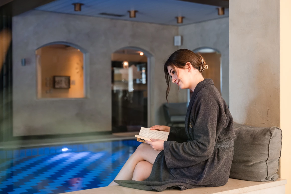 Wellnesshotel: Eine junge Frau liest ein Buch am Rand vom Schwimmbad - Posthotel Rattenberg - Sauna | Spa