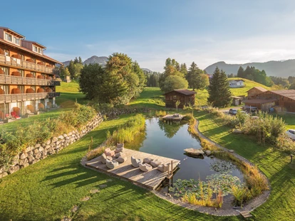 Wellnessurlaub - Fontanella - Das Hotel Oberstdorf hat einen eigenen Naturbadessee! Auf 360 m² schwimmen Sie in türkis-grünem Wasser, völlig ohne chemische Zusätze, entspannen auf der großen Liegewiese und genießen den Blick auf die Allgäuer Bergwelt. - Hotel Oberstdorf