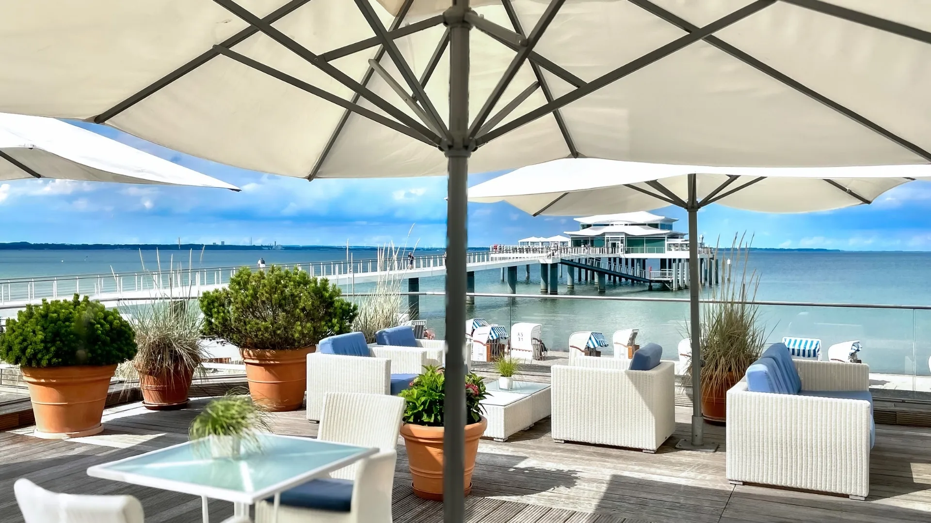 Wellnessurlaub - Wellness mit Kindern - Scharbeutz - Seeterrasse mit Ostseeblick im Grand Hotel Seeschlösschen Timmendorfer Strand mit weißen Möbeln und weißen Sonnenschirmen - Grand Hotel Seeschlösschen Sea Retreat & SPA