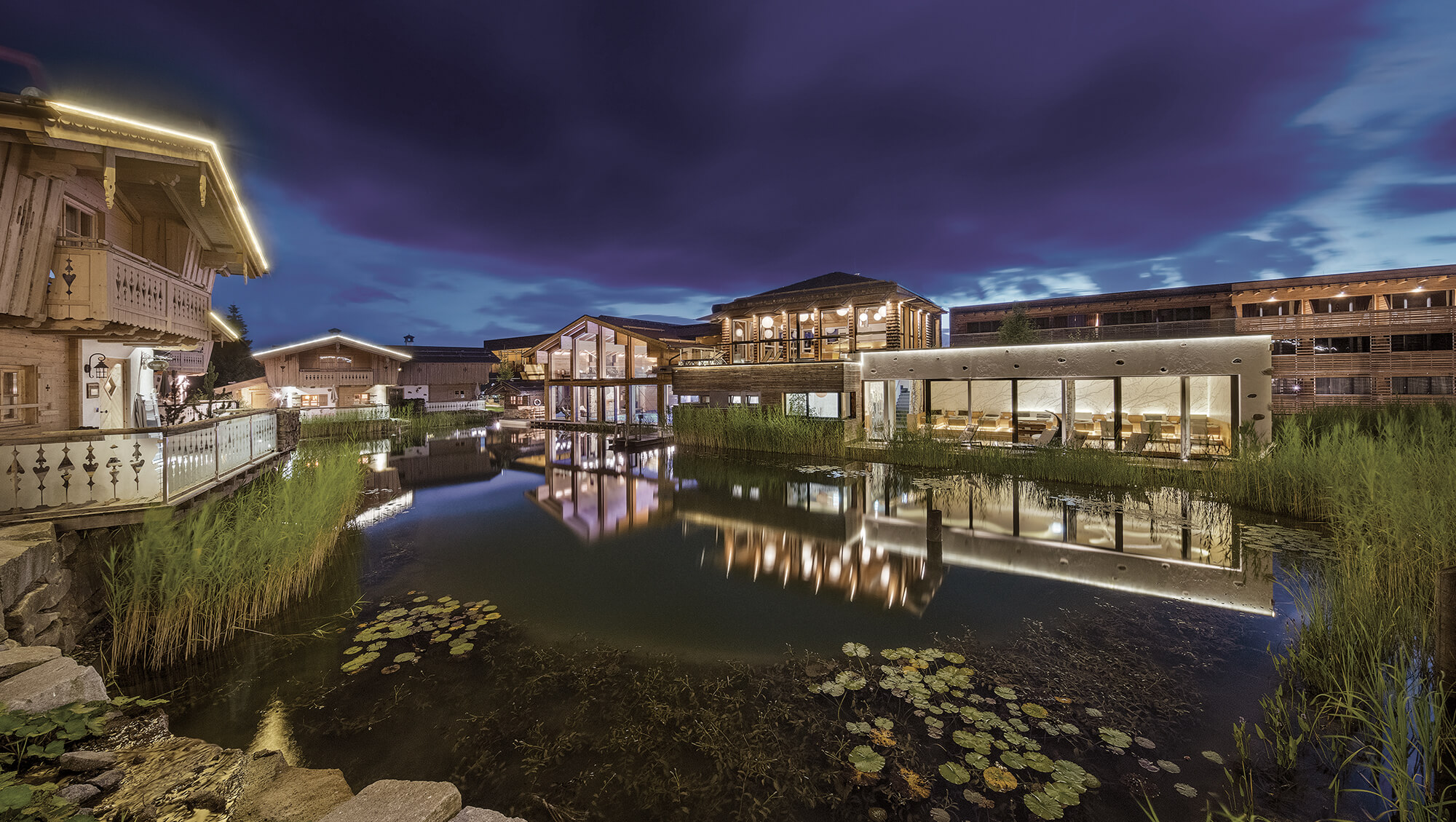 Wellnesshotel: INNs HOLZ Chaletdorf samt Blick auf den Wellnessbreich mit Indoorpool bei Nacht - INNs HOLZ Chaletdorf - Hotel | Umgebung, Wasser
